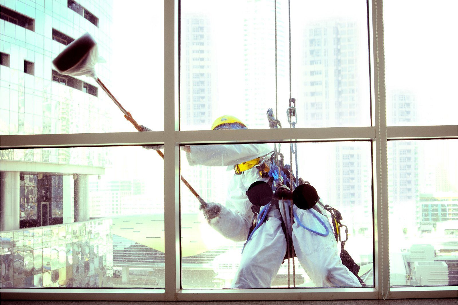 Window washer in safety harness cleans a skyscraper window with a long-handled squeegee.