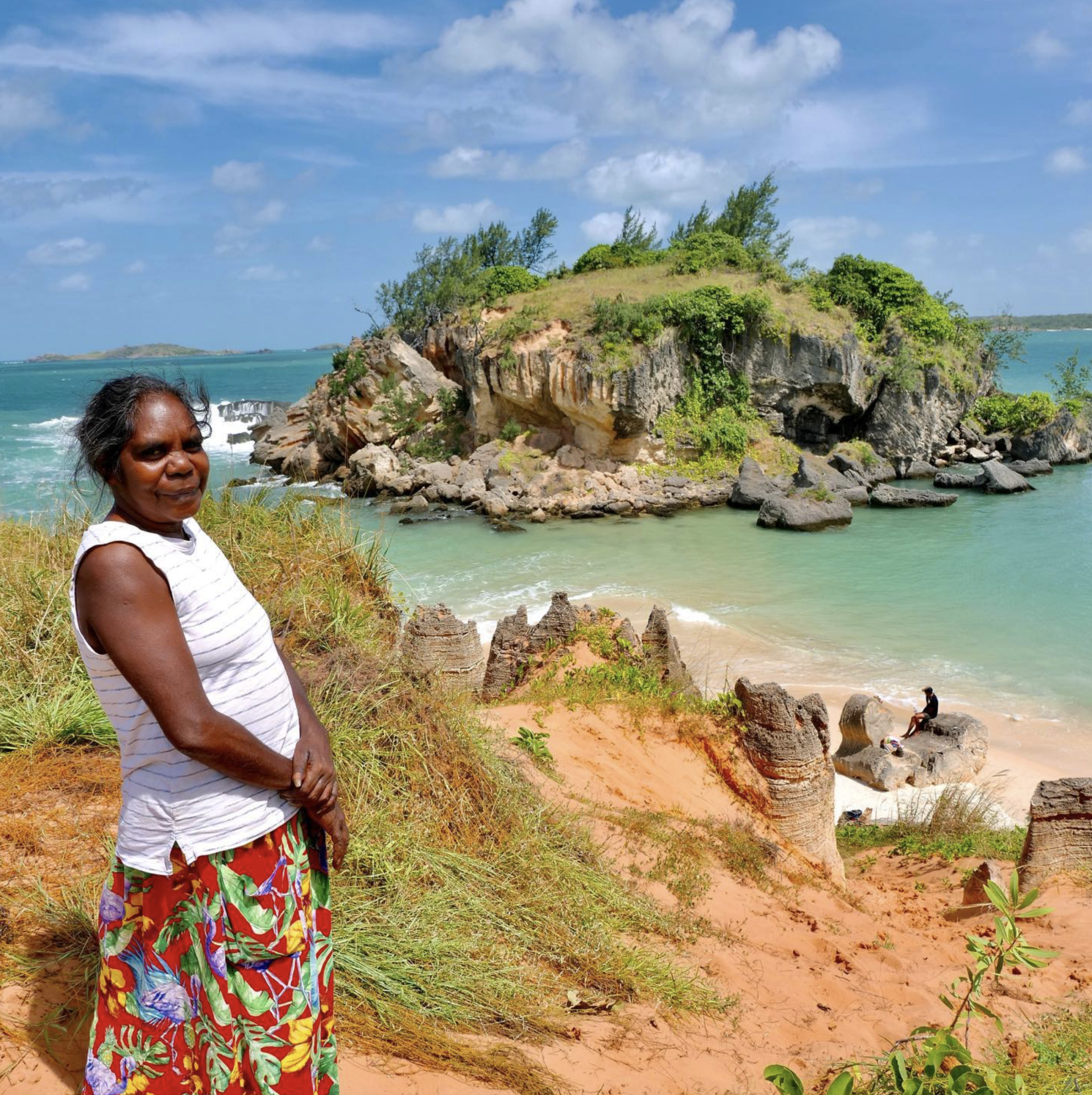 A woman stands on a hill overlooking a small island in the ocean