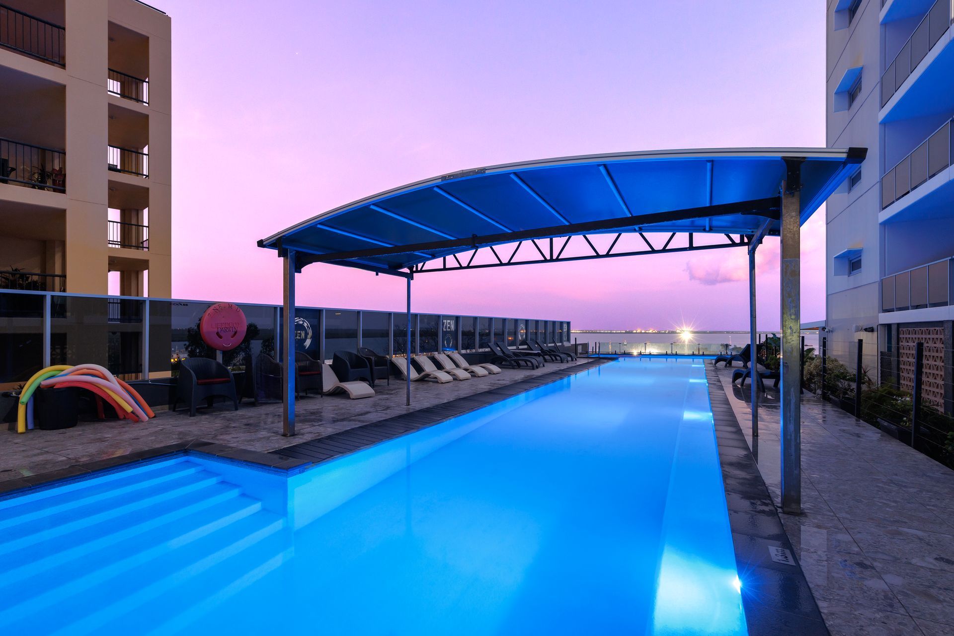 A large swimming pool is lit up at night in front of a building.