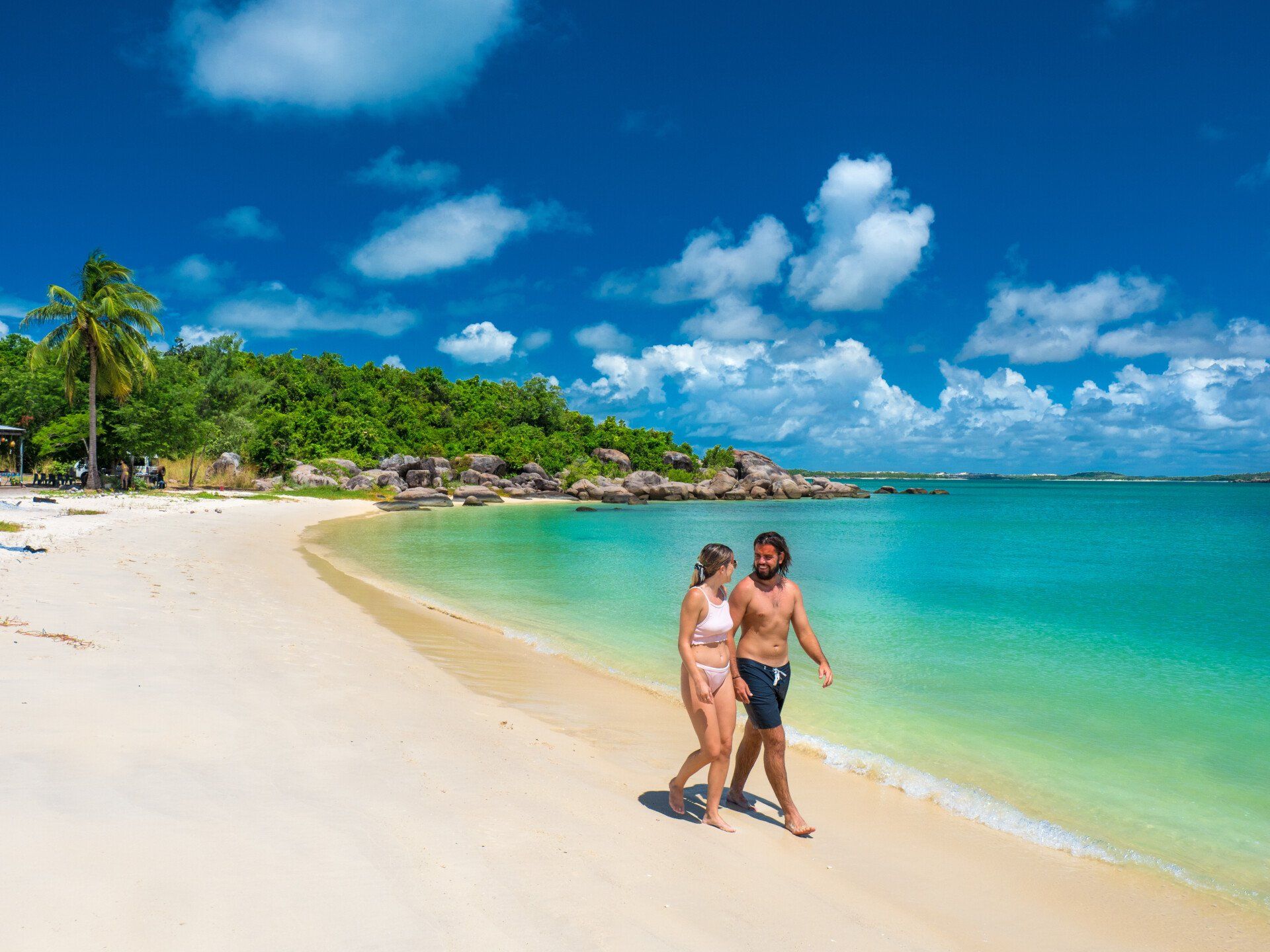 A man and a woman are walking on a tropical beach.