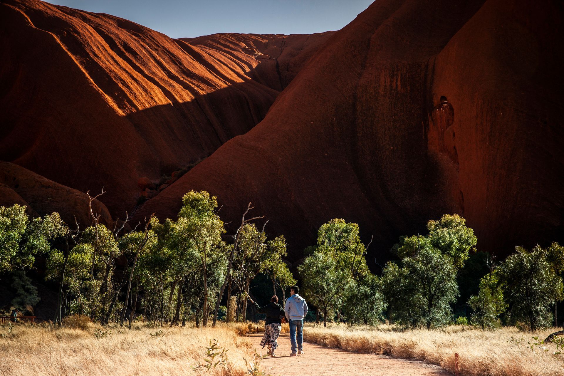 Two people are walking down a dirt path in the desert.