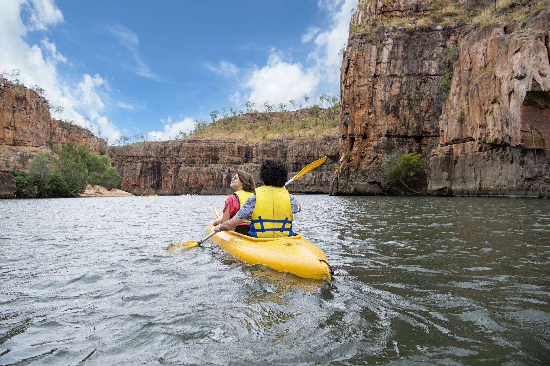 A man and a woman are paddling a yellow kayak on a river.