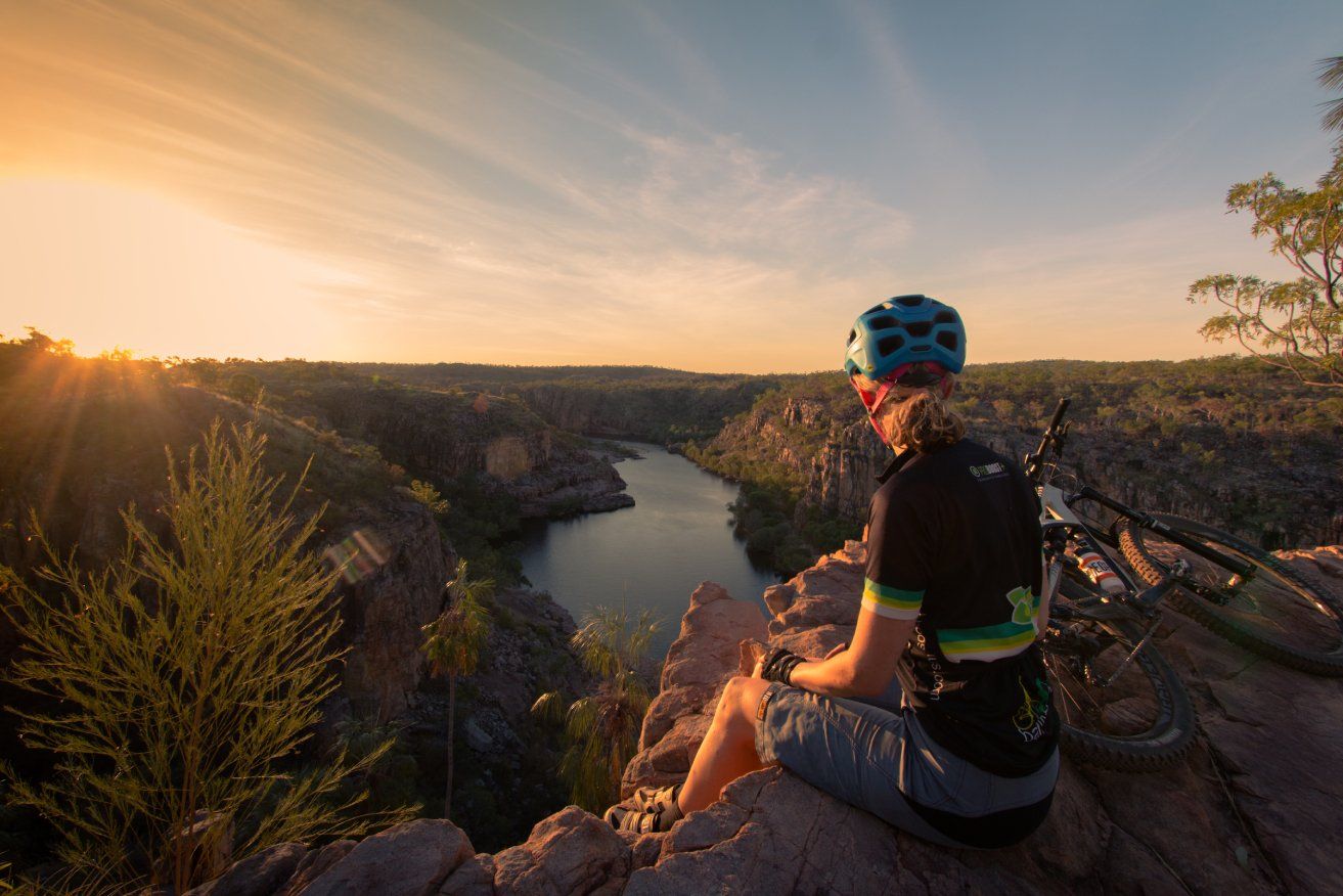 A person is sitting on top of a cliff overlooking a river.