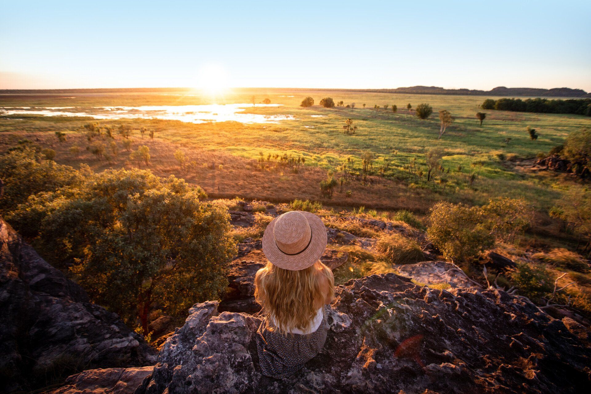 A woman is sitting on top of a rock looking at the sunset.