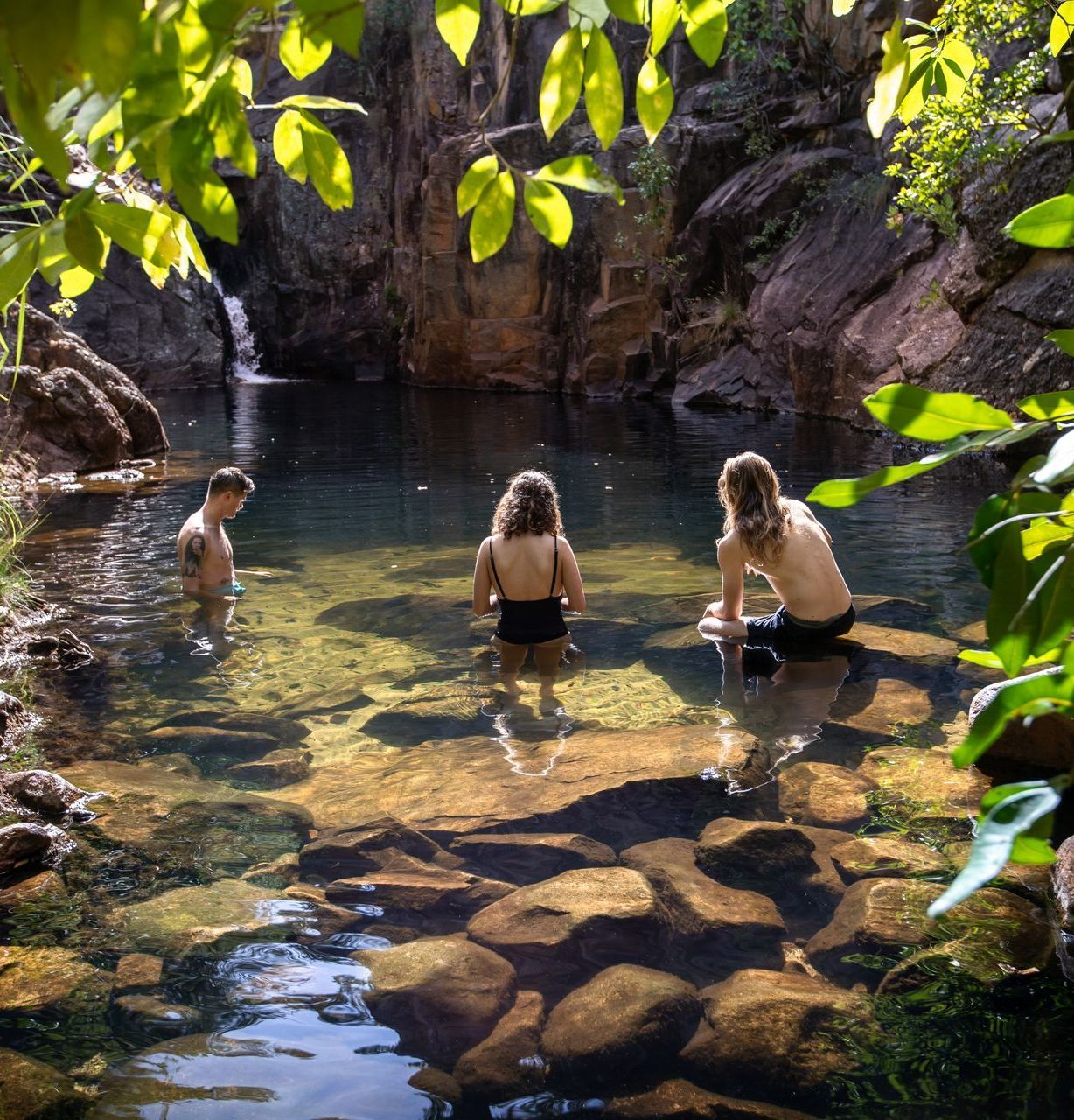 Three people are swimming in a river surrounded by rocks