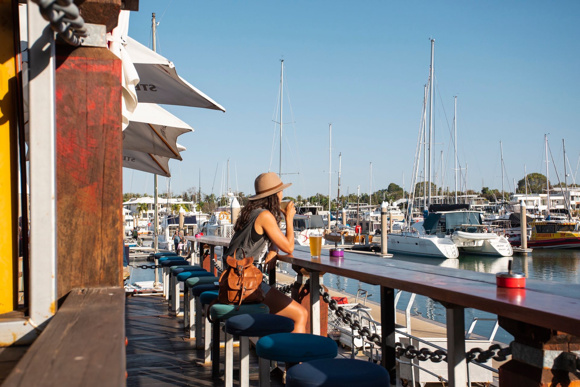 A woman is sitting at a bar looking at boats in a marina.