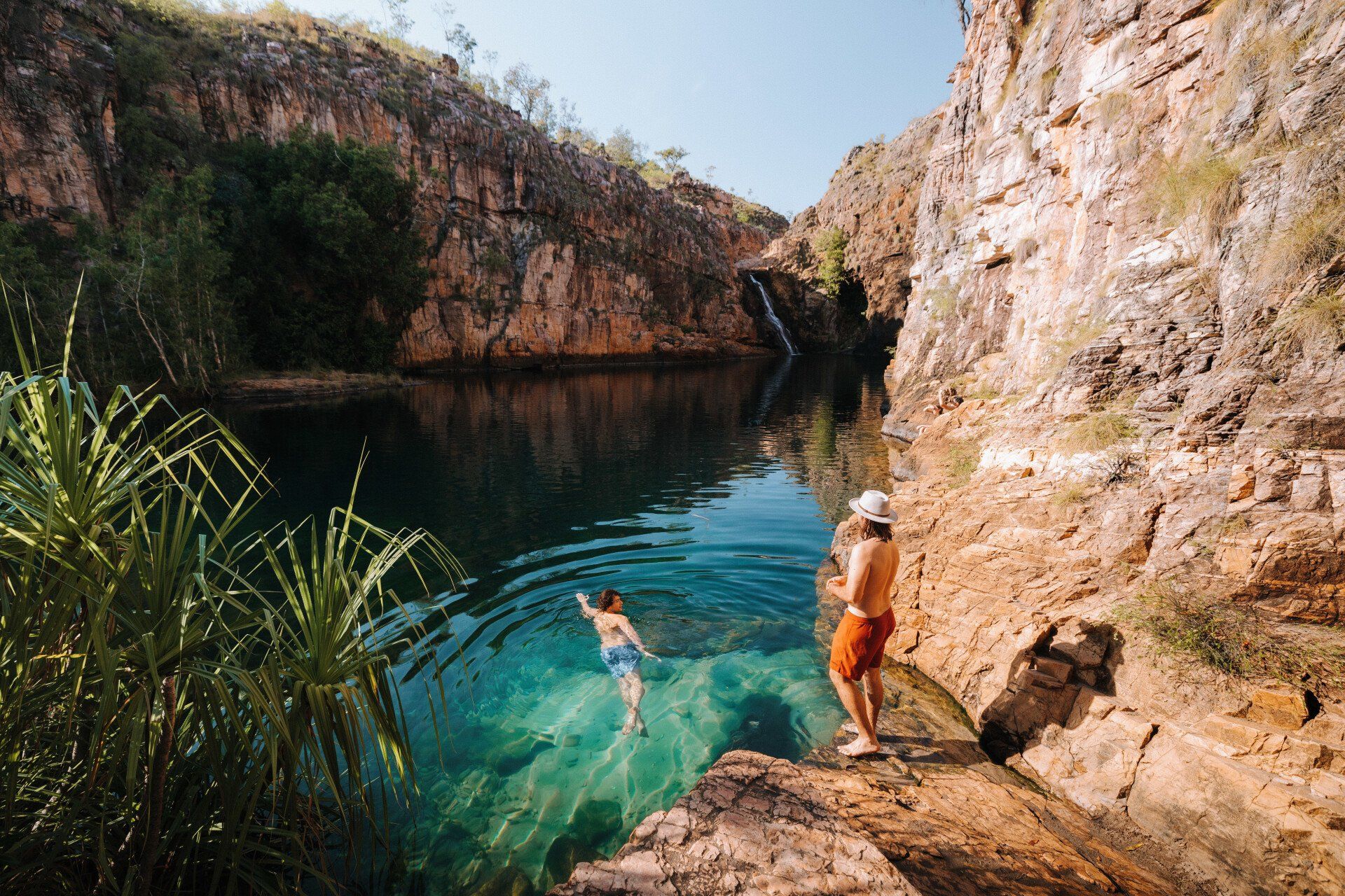 Two people are swimming in a lake surrounded by rocks.
