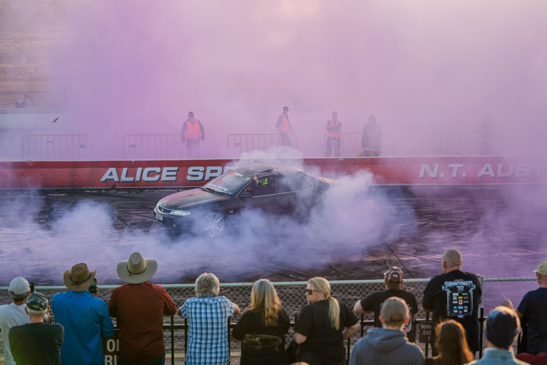 A group of people are watching a car do a burnout at a race track.
