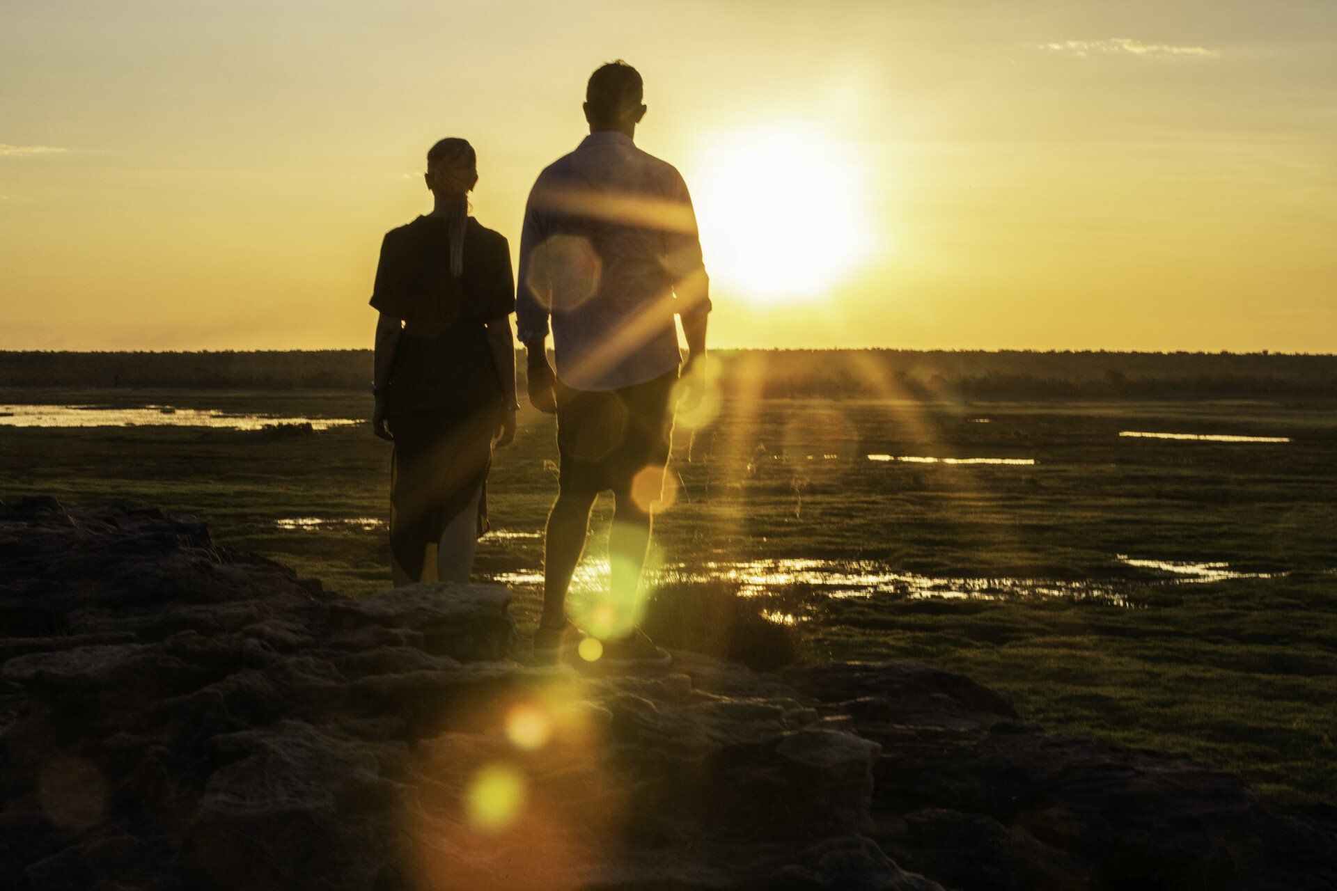 Two men are walking on a beach at sunset.