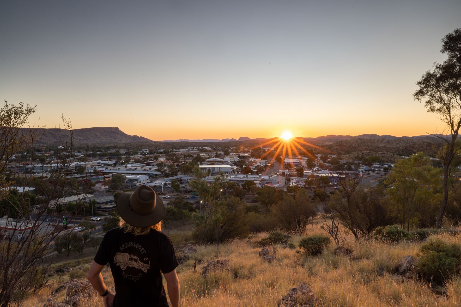 A person is standing on top of a hill looking at the sunset over a city.