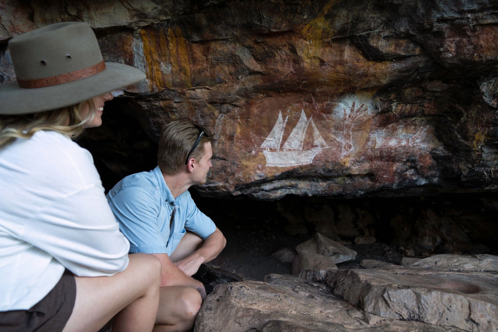 A man and a woman are looking at a painting on a rock wall.