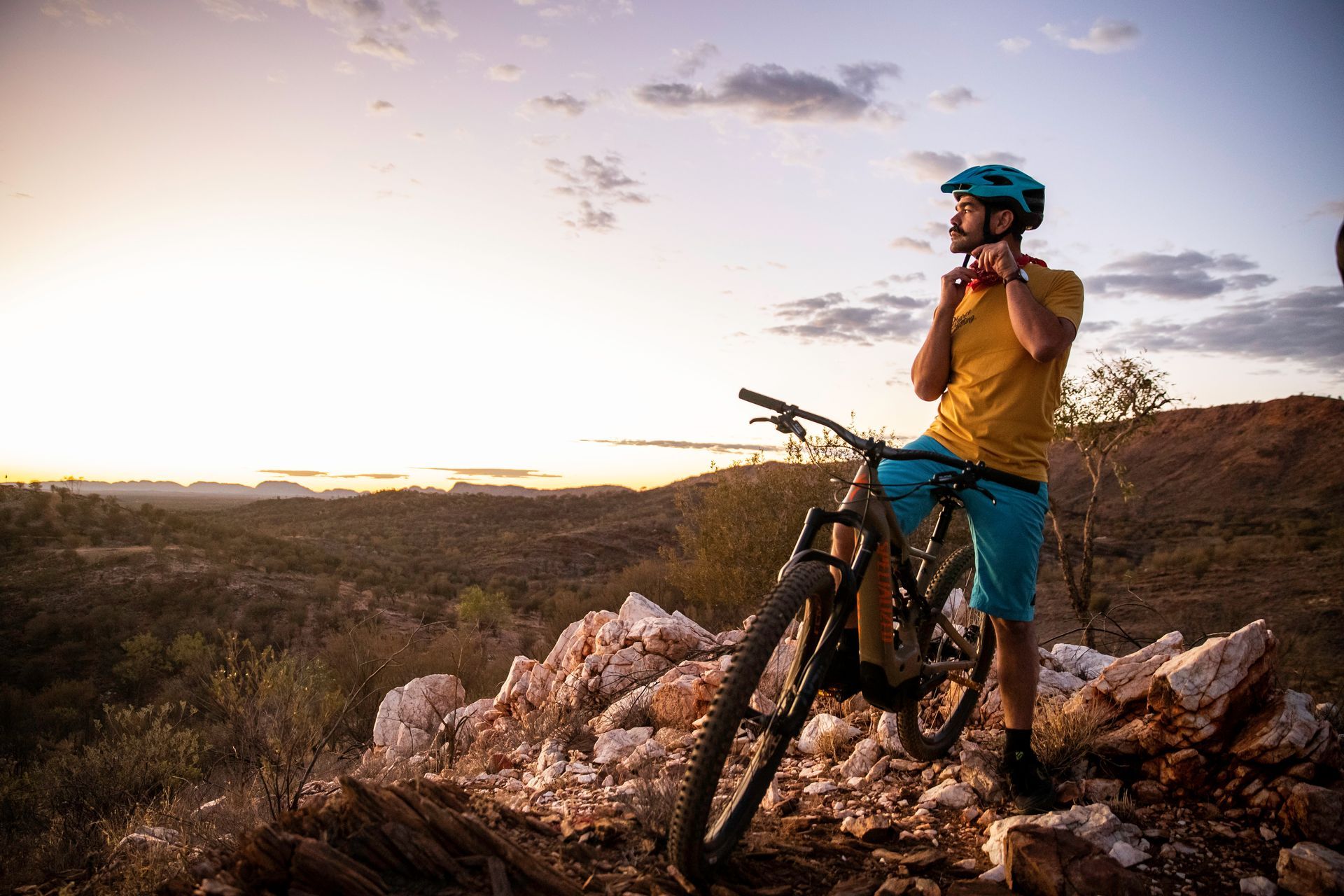A man is standing next to a mountain bike on top of a rocky hill.
