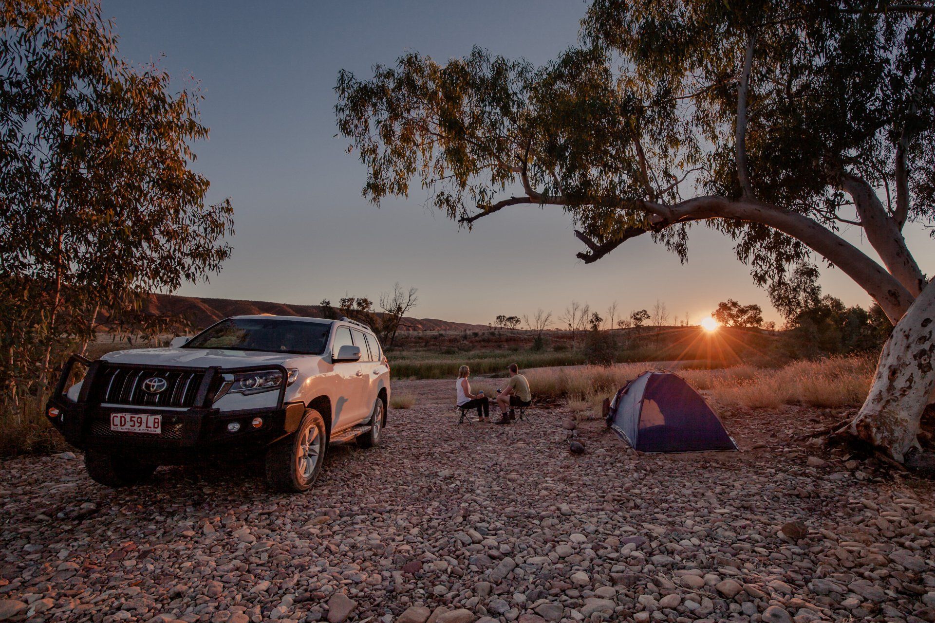 A car is parked next to a tent in a rocky area.