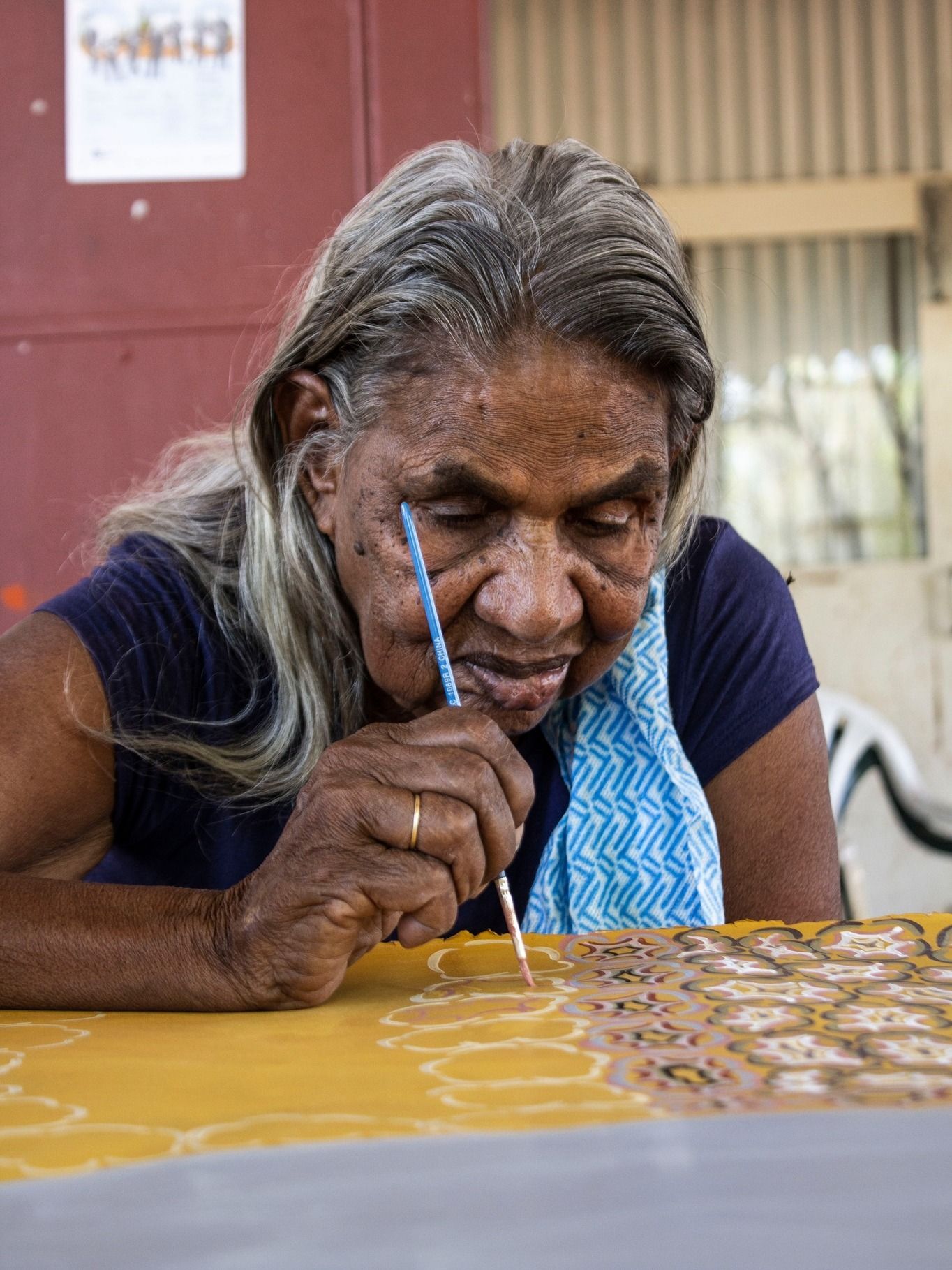 A woman is sitting at a table painting with a brush.