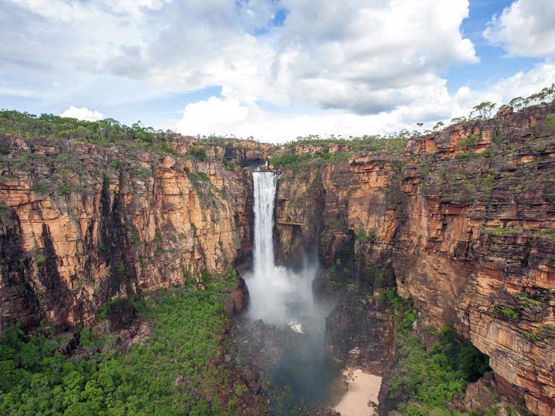 There is a waterfall in the middle of a canyon surrounded by trees.