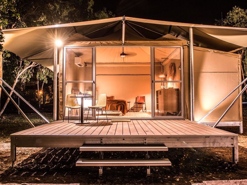 A tent with a wooden deck and stairs is lit up at night.