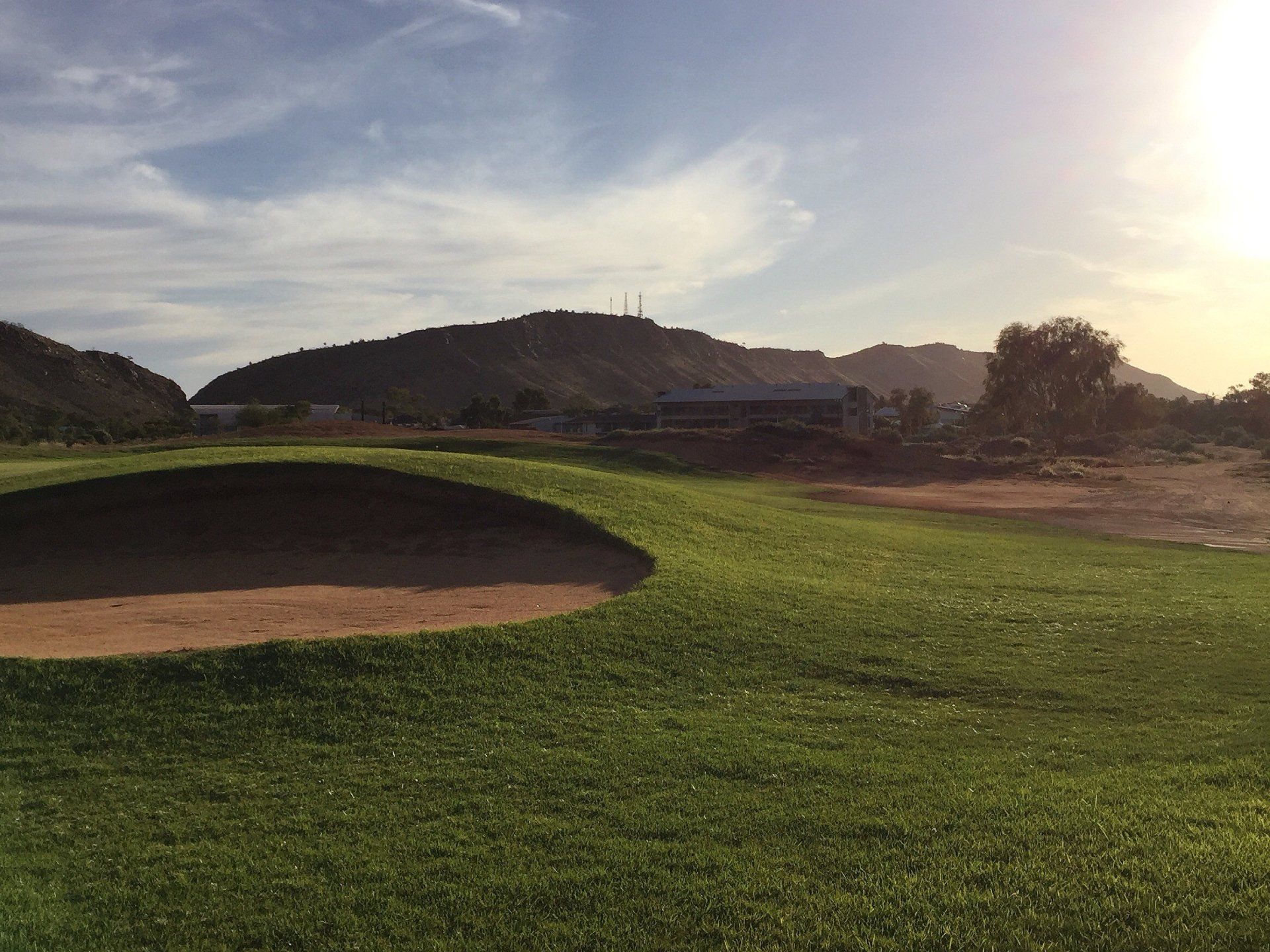 A golf course with mountains in the background and a bunker in the foreground.