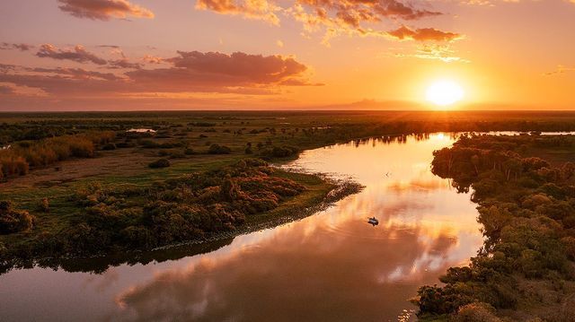 The sun is setting over a river surrounded by trees.