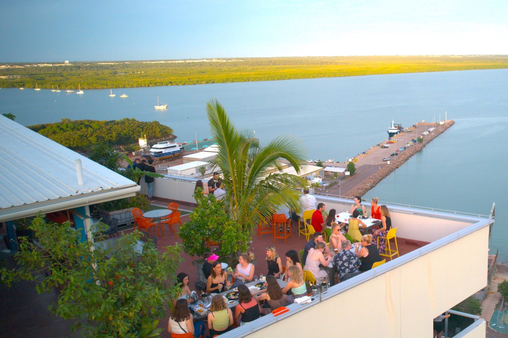 A group of people are sitting at tables on a roof overlooking a body of water.