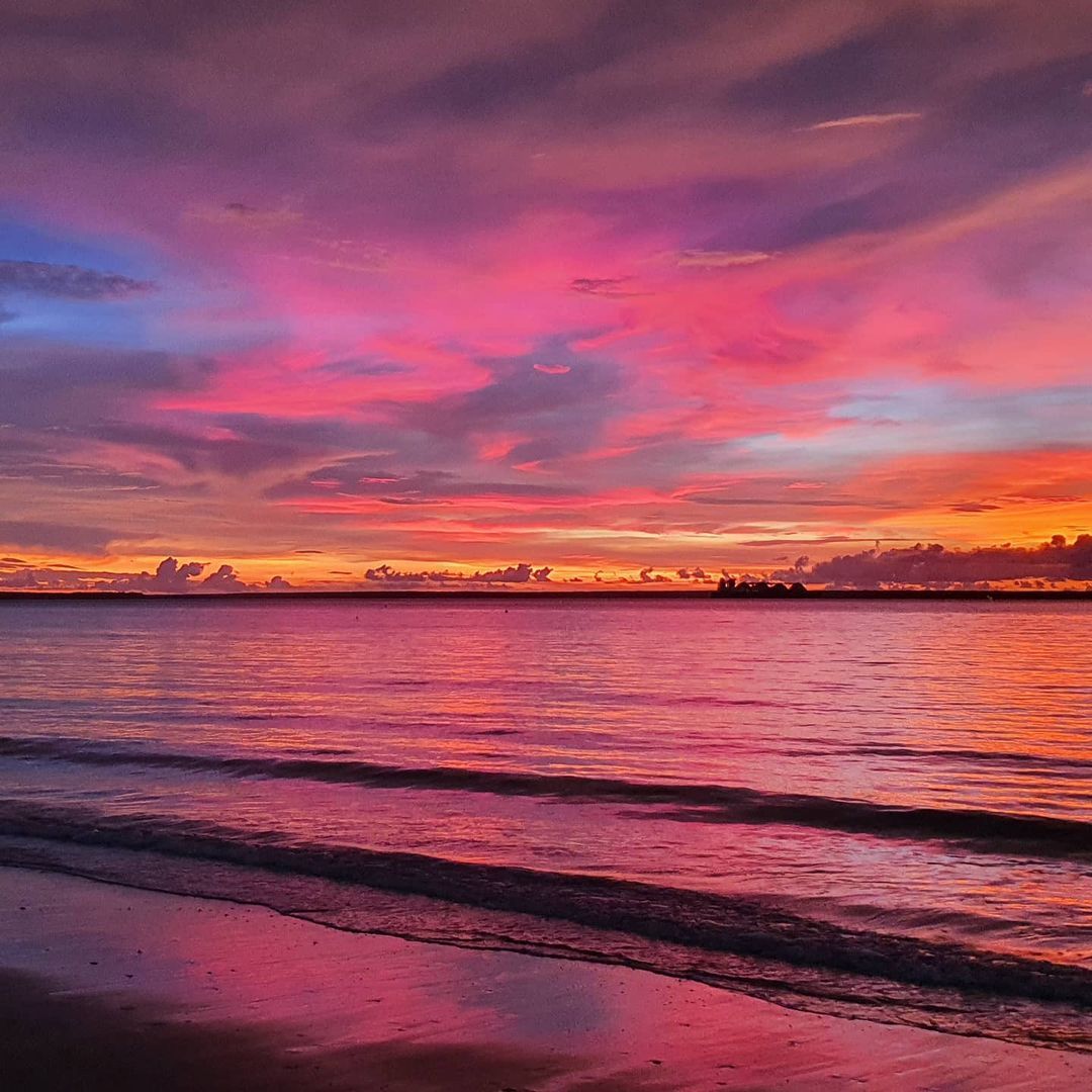 A colorful sunset over a body of water with a beach in the foreground.