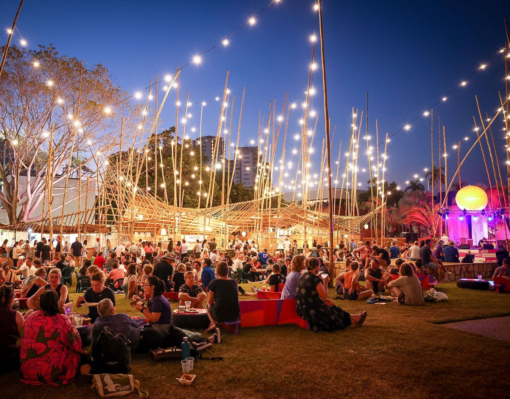 A large group of people are sitting in the grass at a festival.