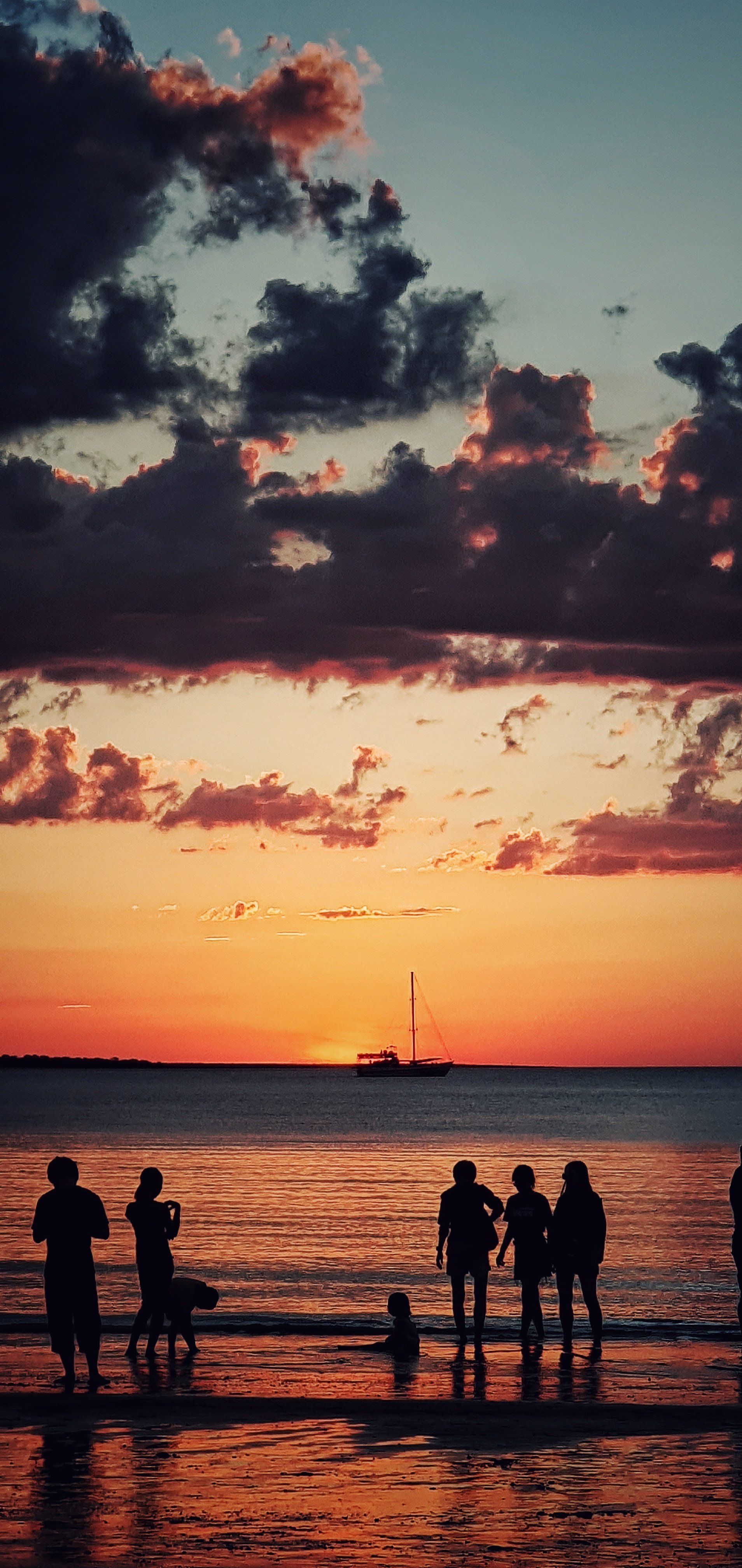 A group of people are standing on a beach at sunset.
