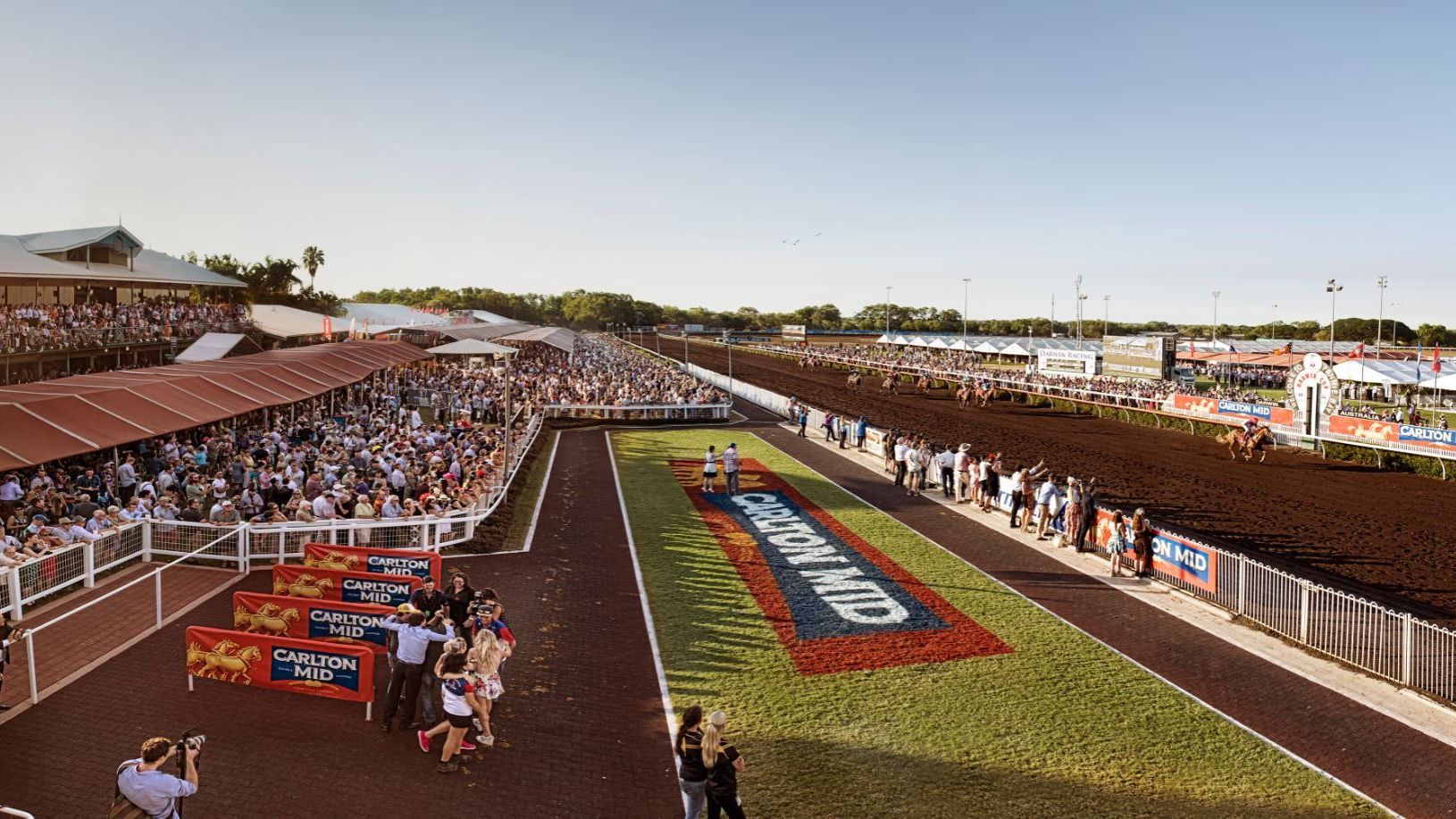 A large crowd of people are watching a race at a race track.