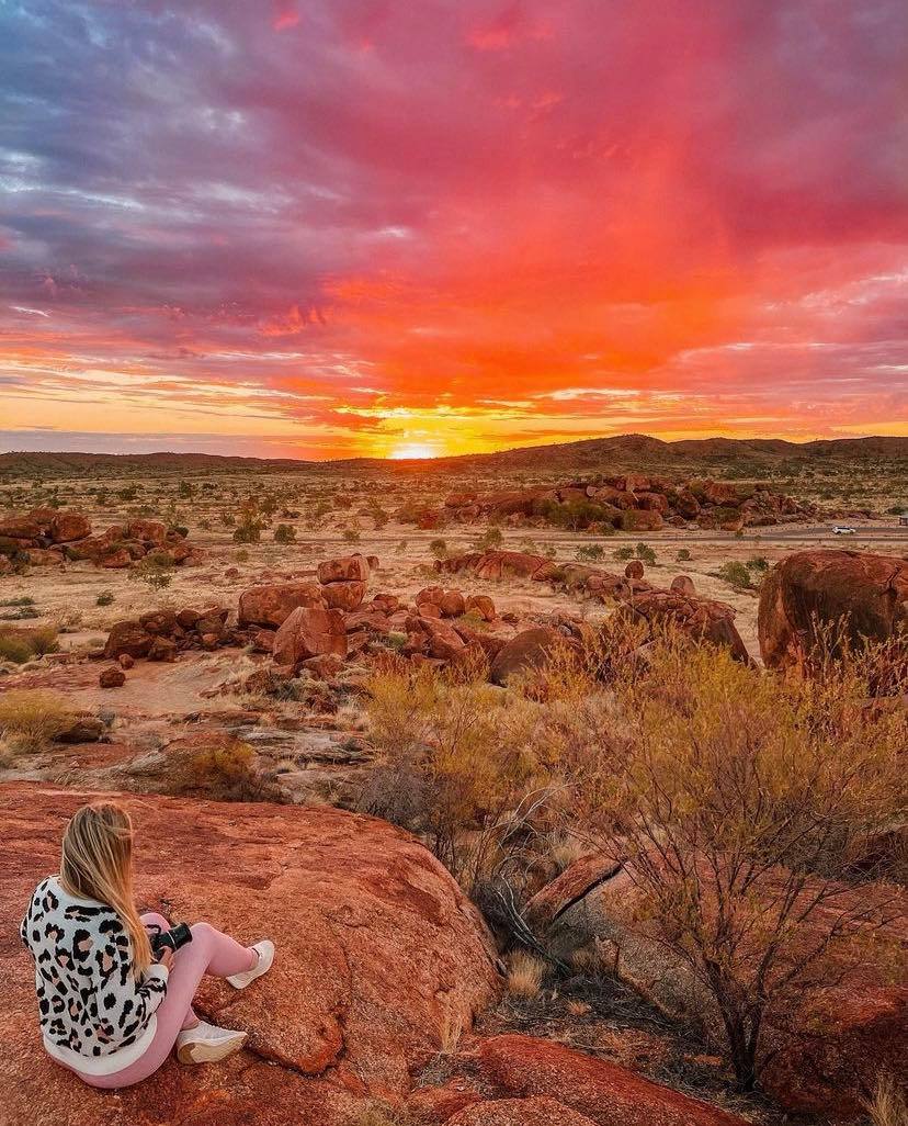 A woman is sitting on a rock watching the sunset in the desert.