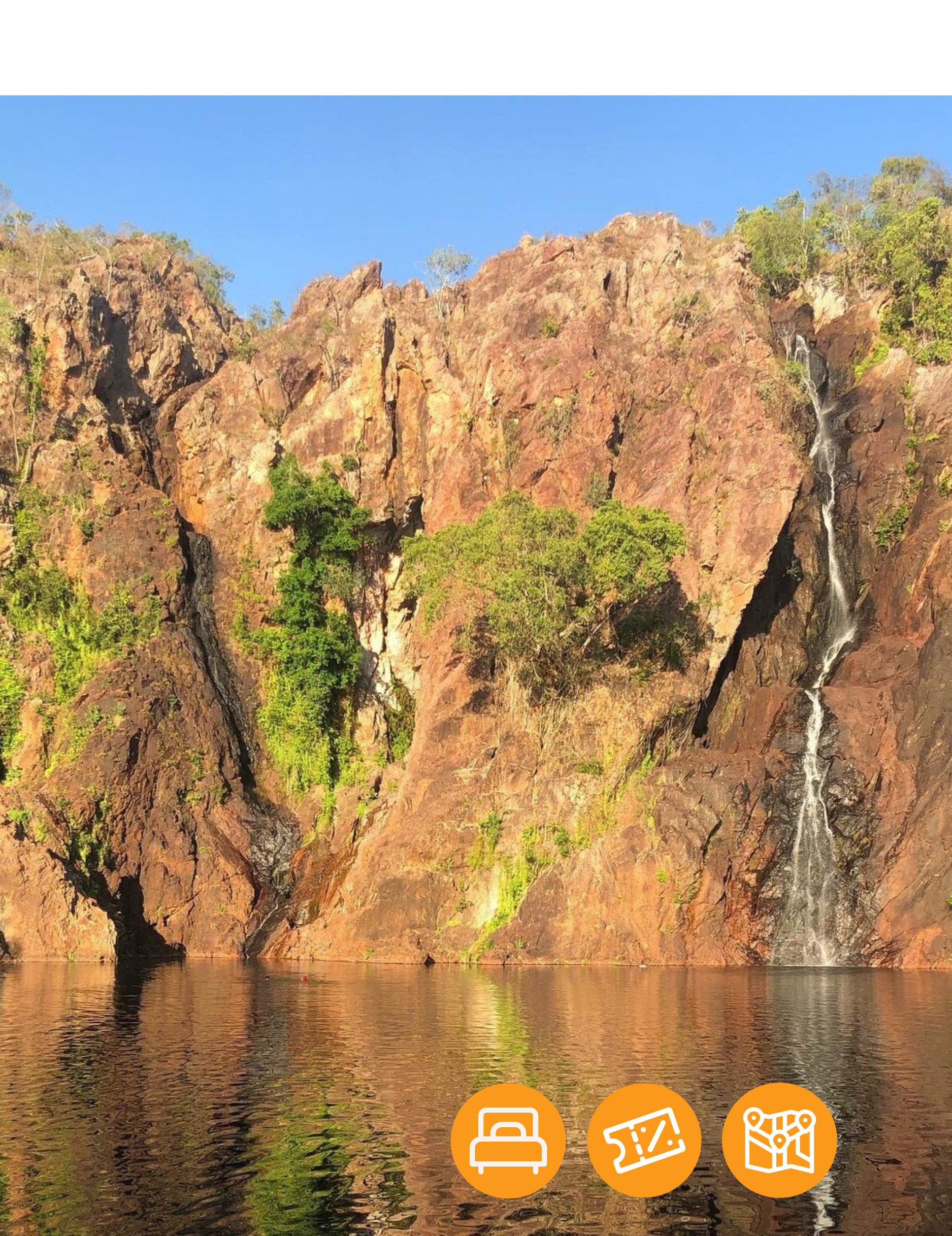 A waterfall is surrounded by rocks and trees next to a body of water.