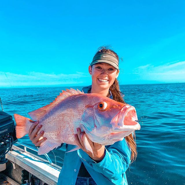 A woman is holding a large fish on a boat in the ocean.