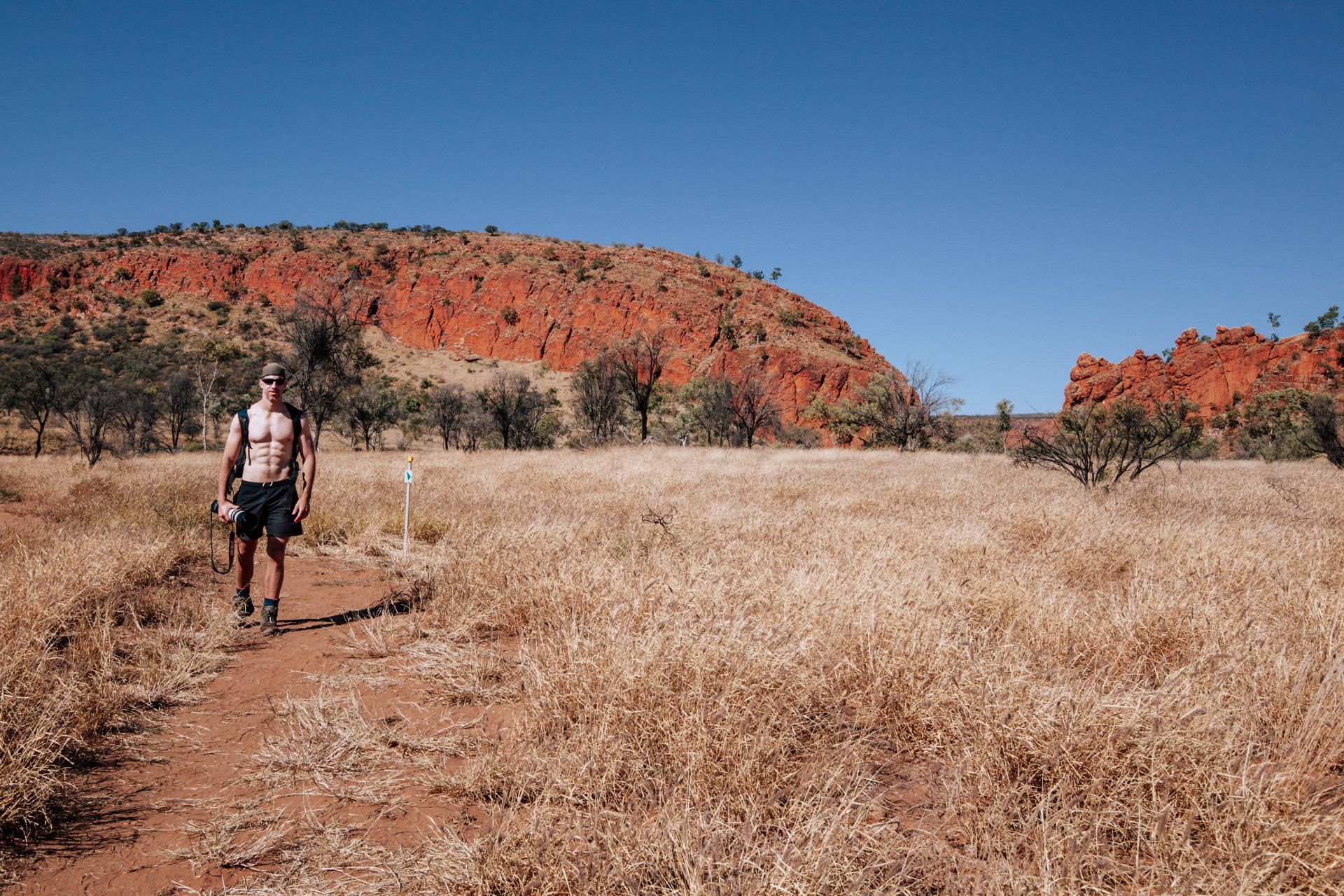 A man without a shirt is walking down a dirt path in the desert.