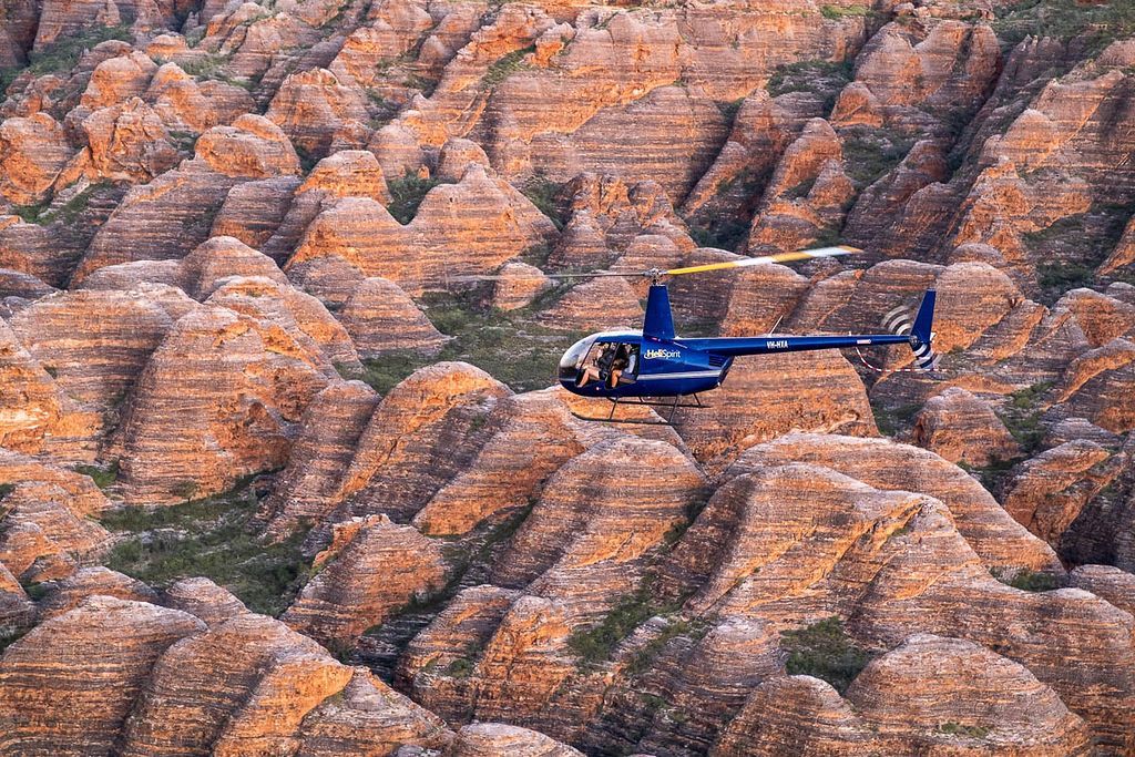 A blue helicopter is flying over a rocky landscape.