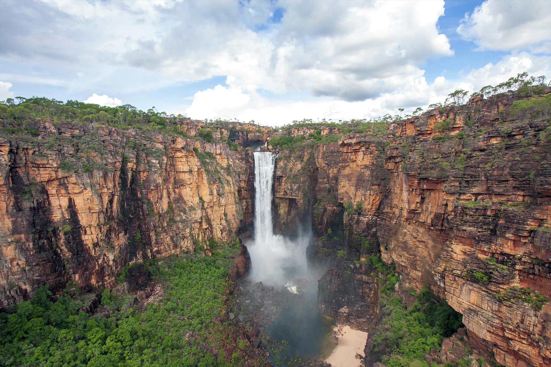 An aerial view of a waterfall in the middle of a canyon surrounded by trees.