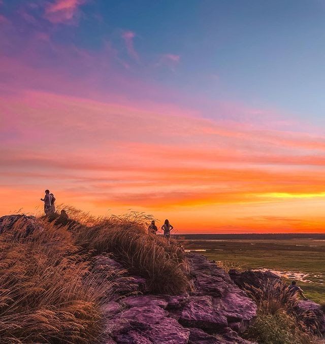 A group of people are standing on top of a rocky hill at sunset.