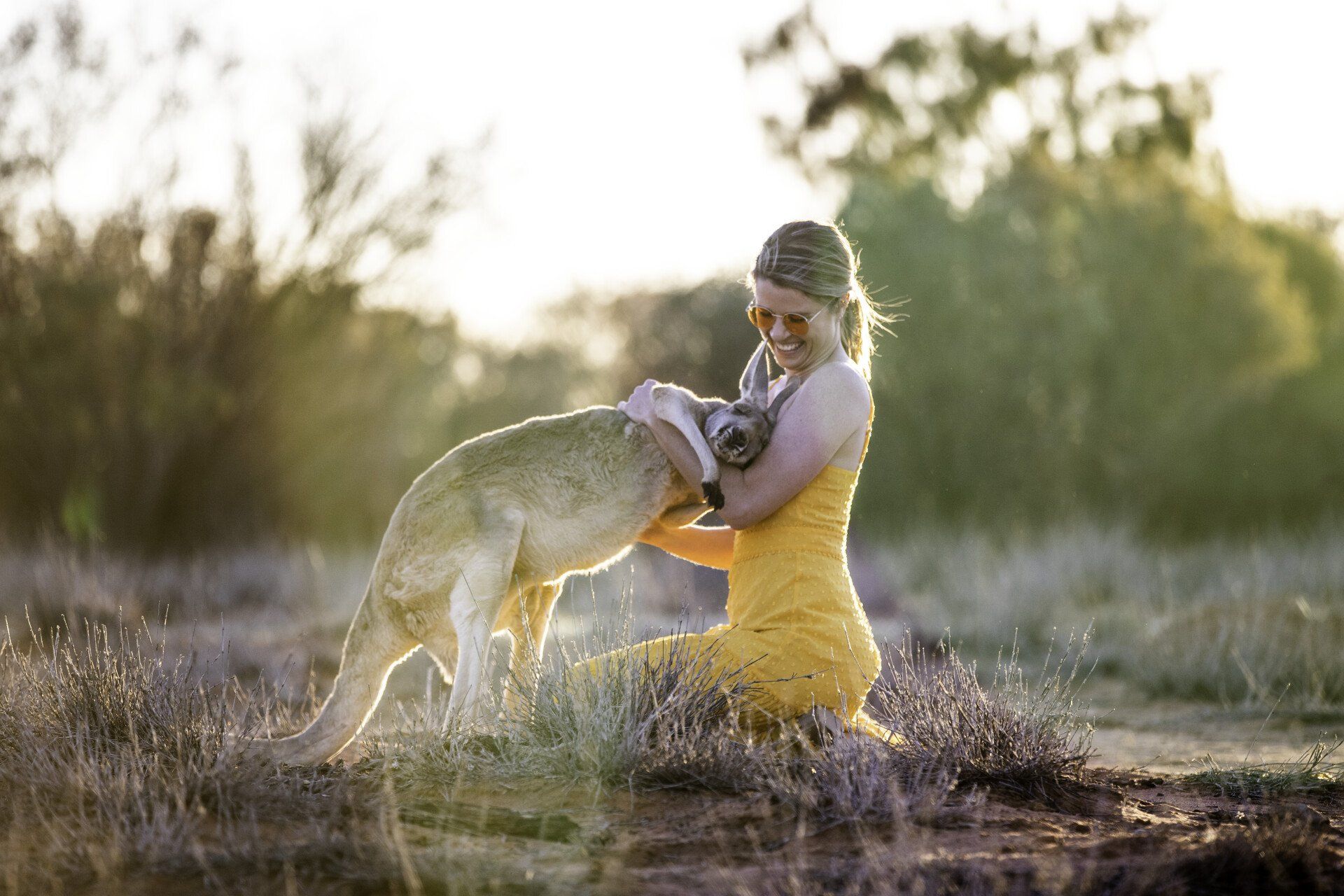 A woman is kneeling down next to a kangaroo in a field.