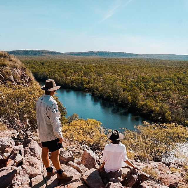 A man and a woman are sitting on a rock overlooking a river.
