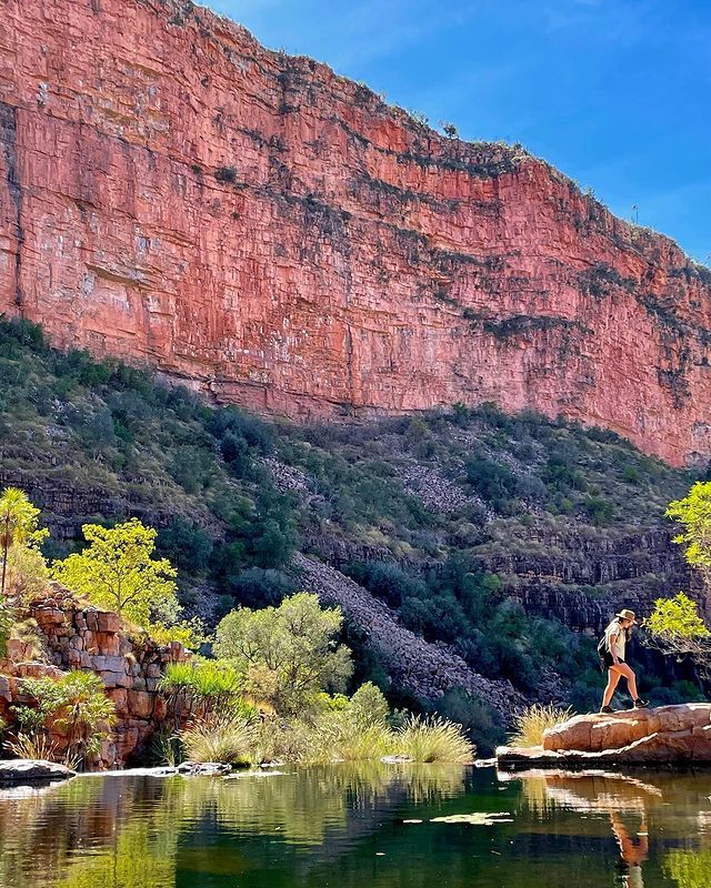 A person is standing on a rock next to a lake with a mountain in the background.