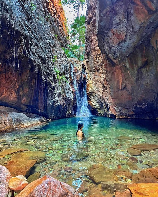 A person is swimming in a pool next to a waterfall.