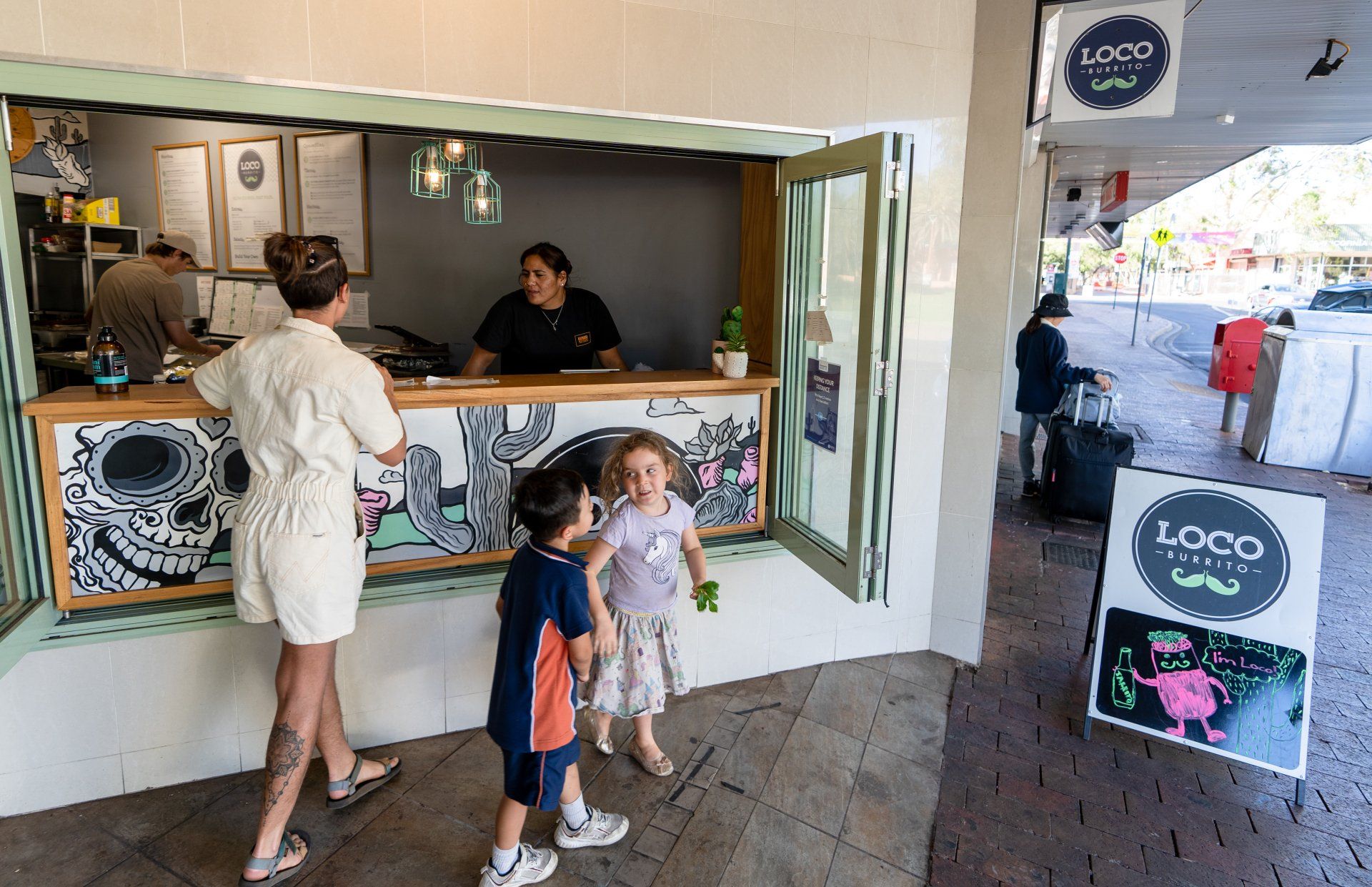 A woman and two children are standing in front of a restaurant counter.