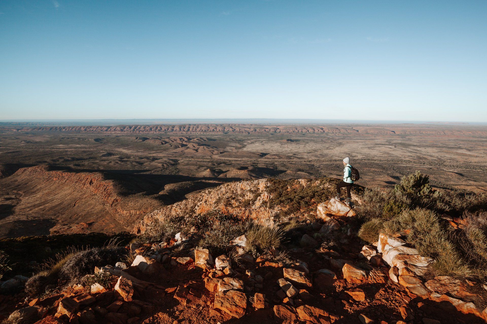 A person is standing on top of a rocky hill overlooking a desert landscape.