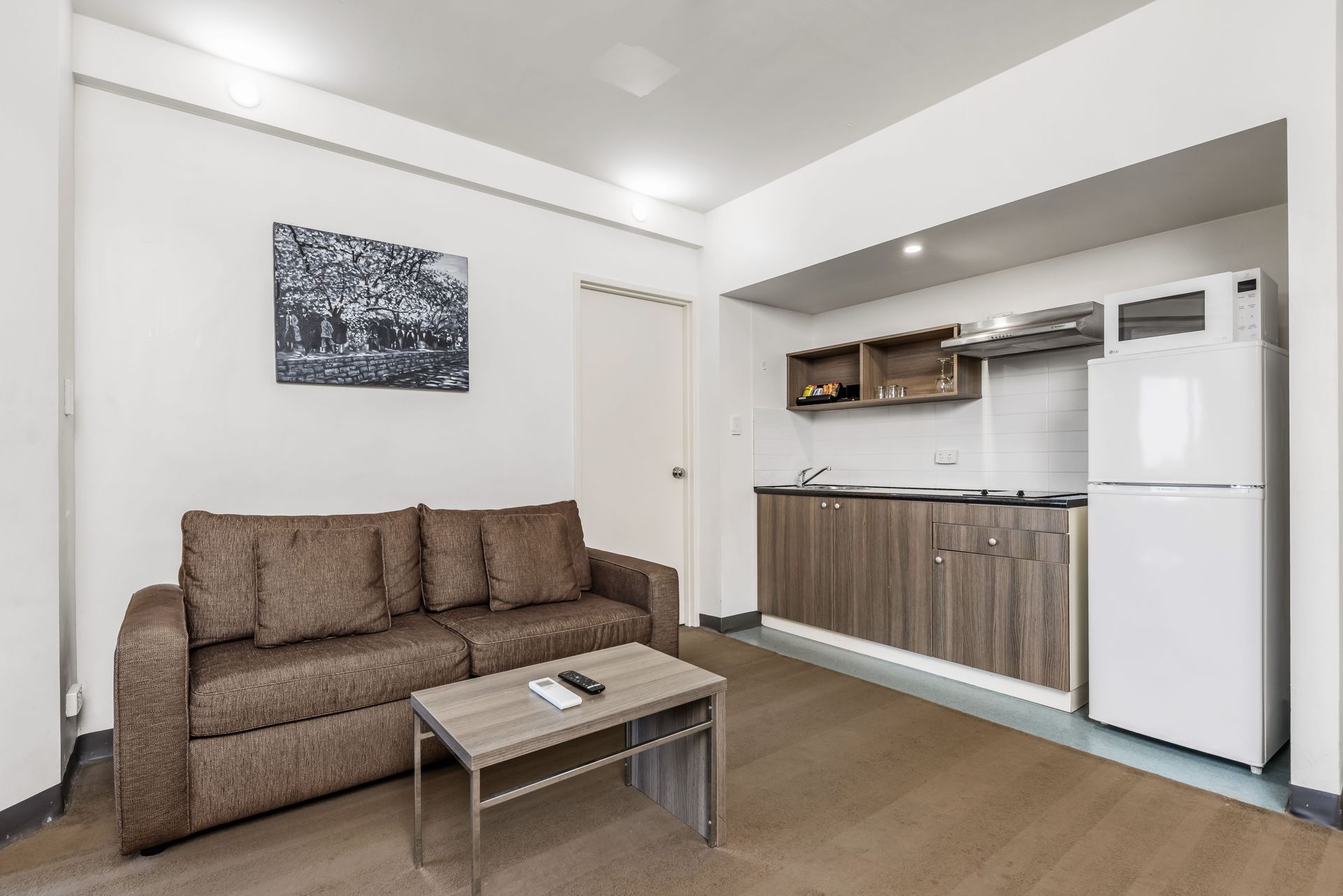 A living room with a couch , table , refrigerator and kitchen.