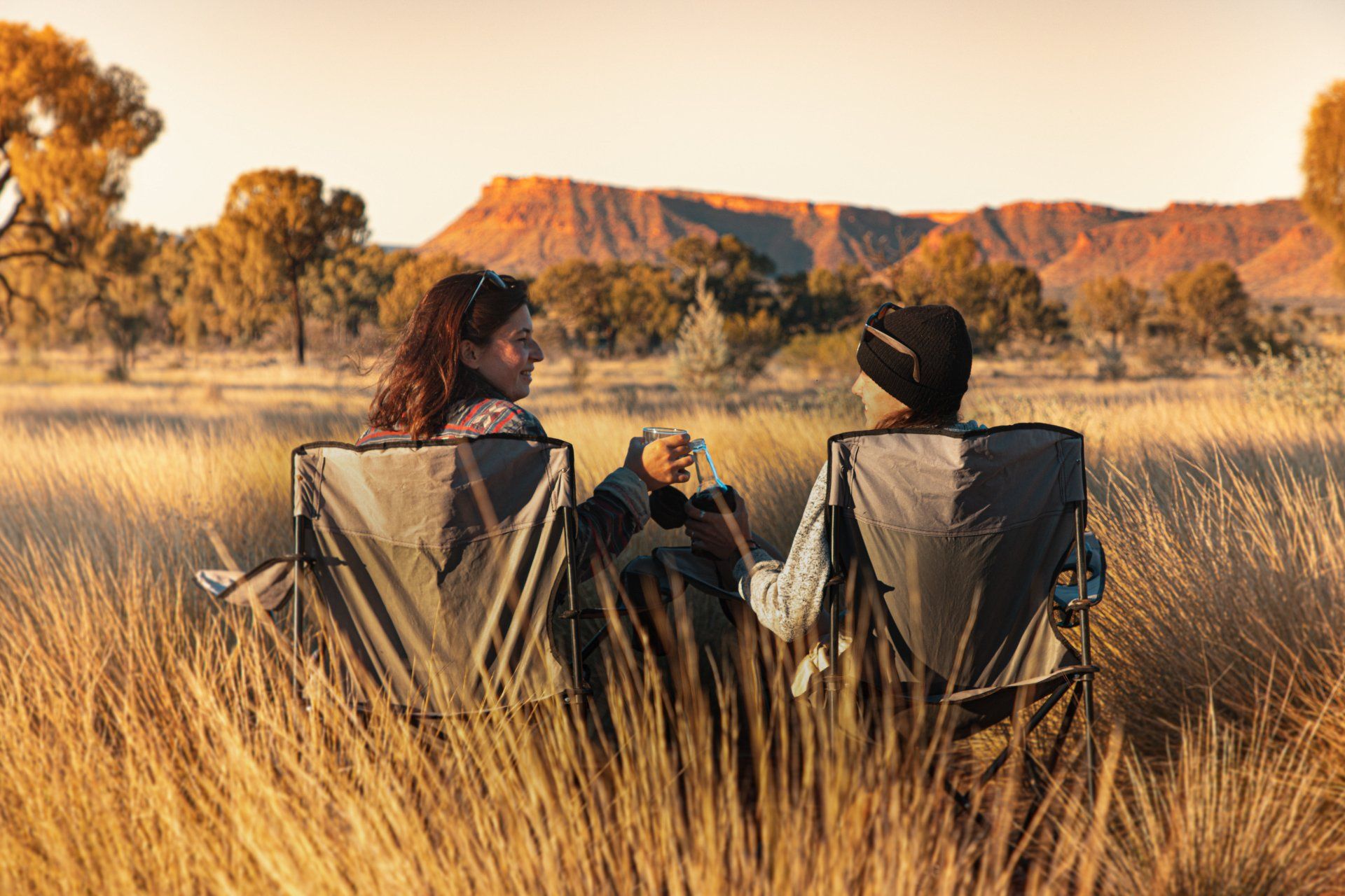 Two people are sitting in chairs in a field looking at a mountain.