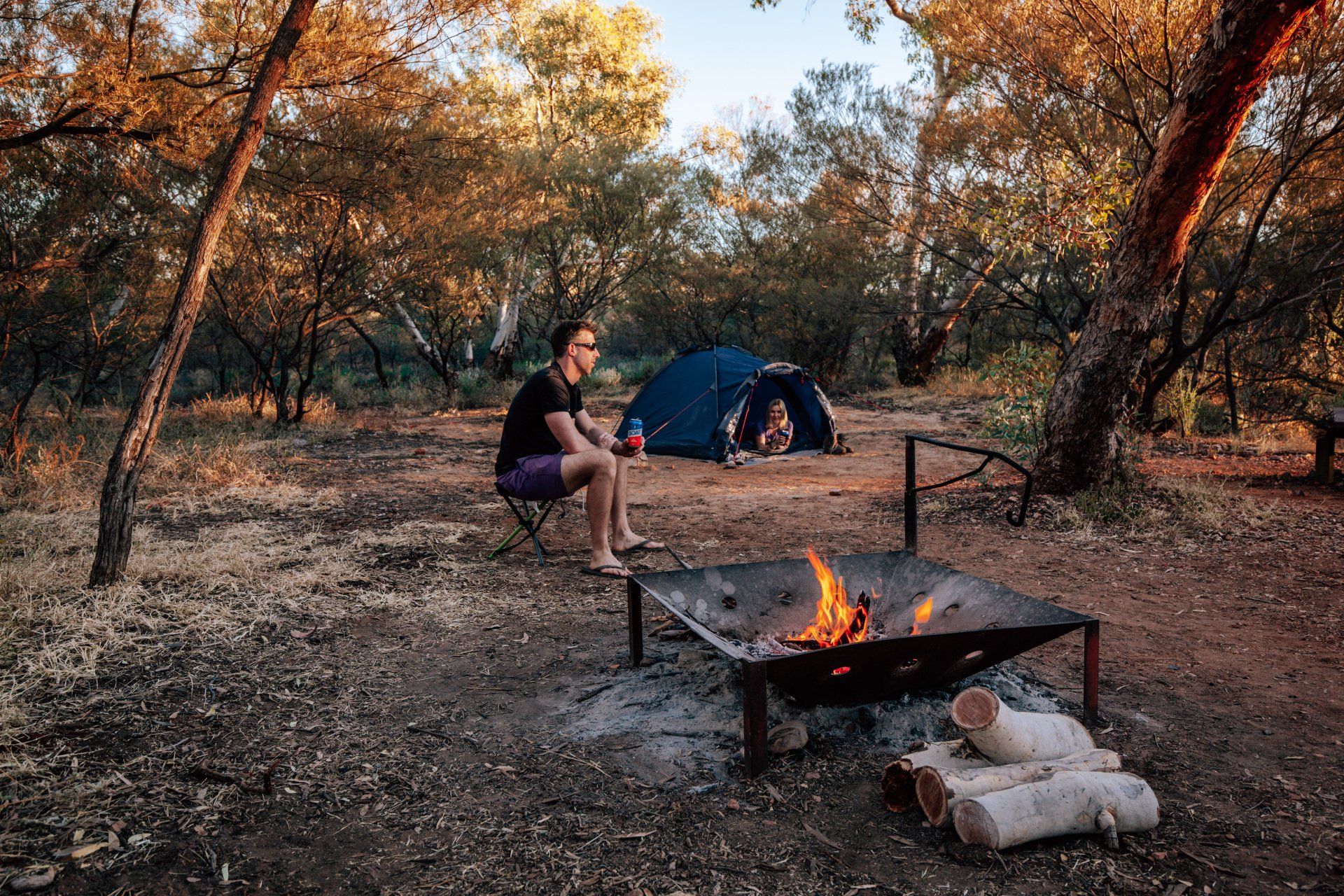 A man is sitting in front of a campfire in the woods.