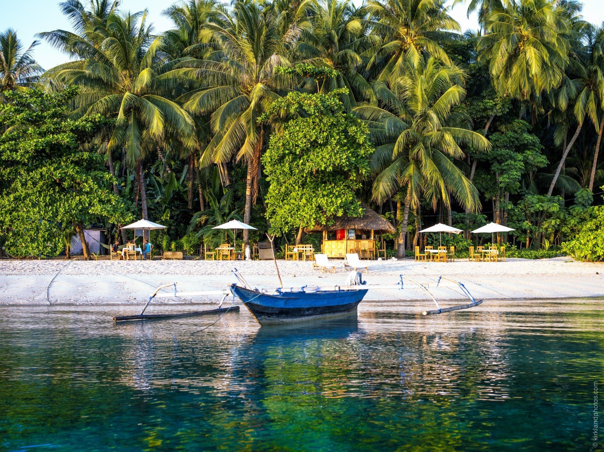 A boat is floating on the water near a beach surrounded by palm trees.