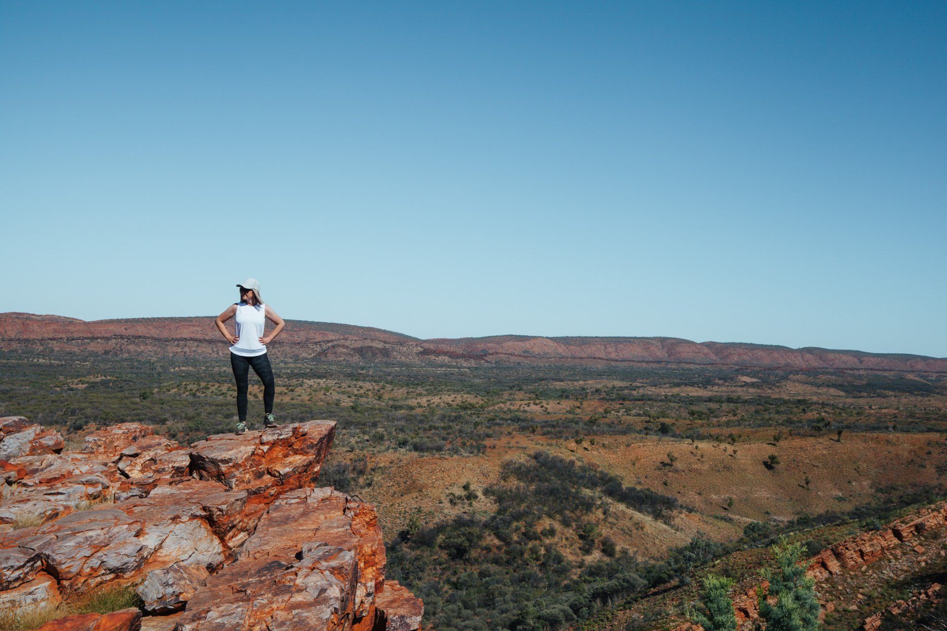 A woman is standing on top of a rocky cliff overlooking a valley.