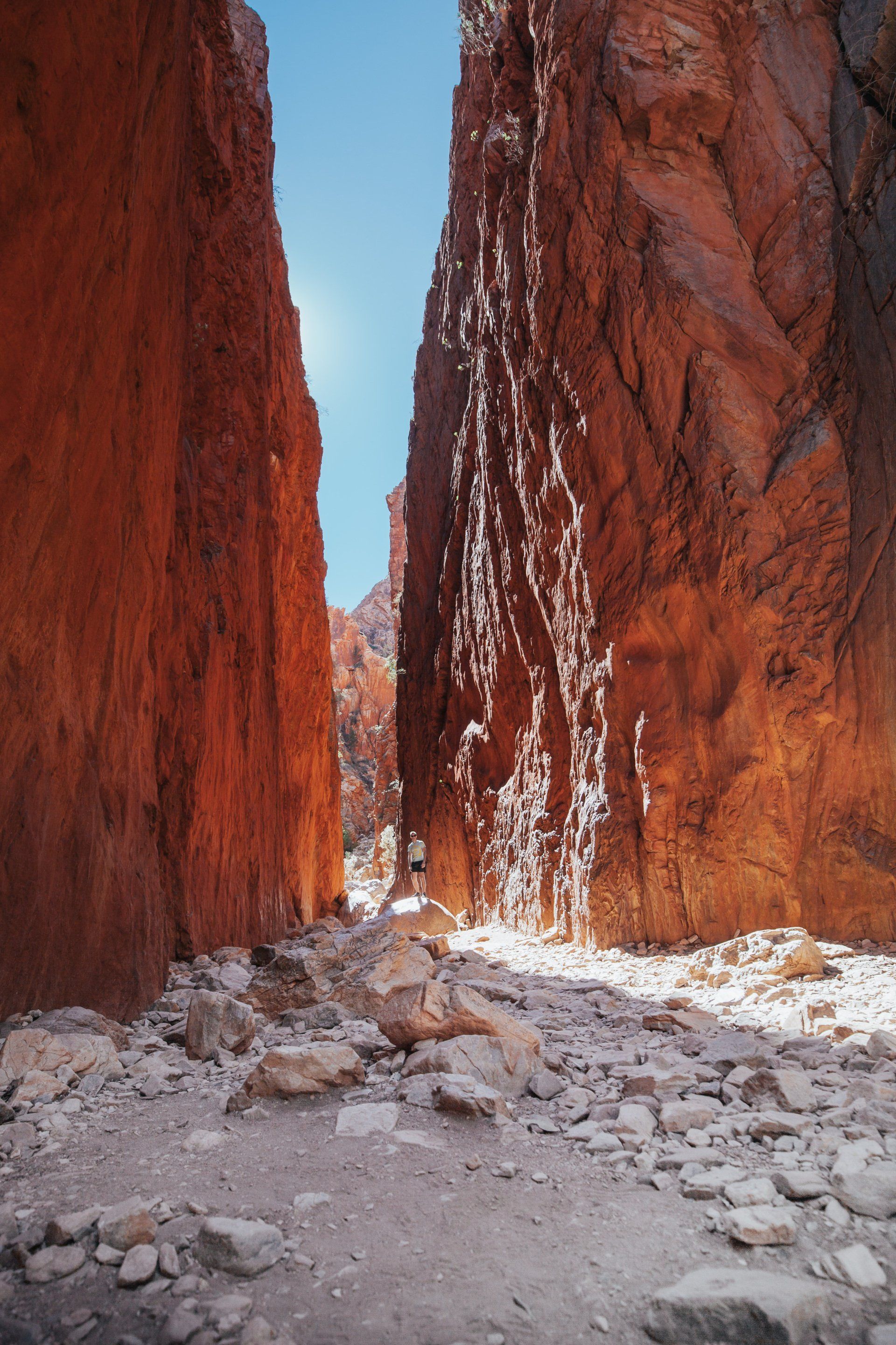 A person is standing in the middle of a canyon between two rocky cliffs.