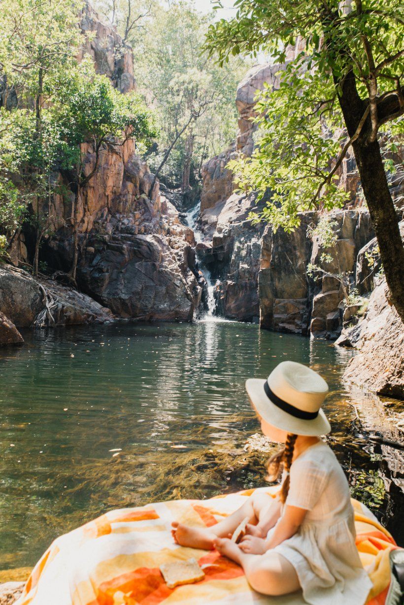 A woman is sitting on a blanket near a waterfall.