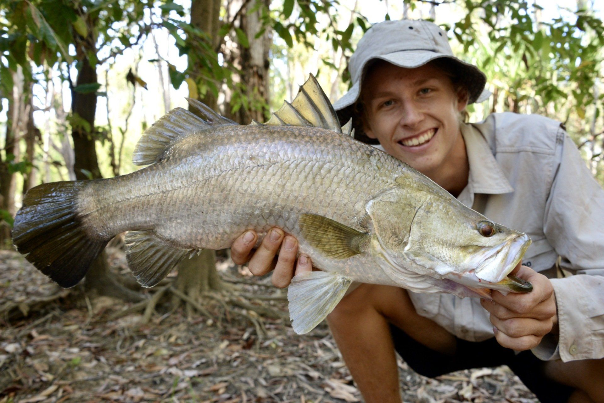 A man is kneeling down holding a large fish in his hands.