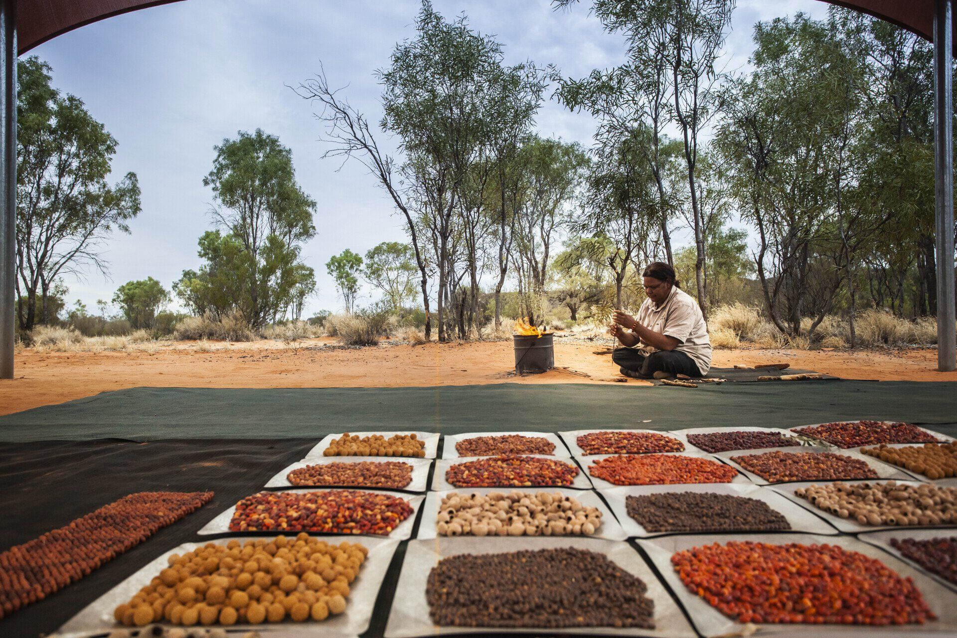A man is sitting on the ground surrounded by plates of food.