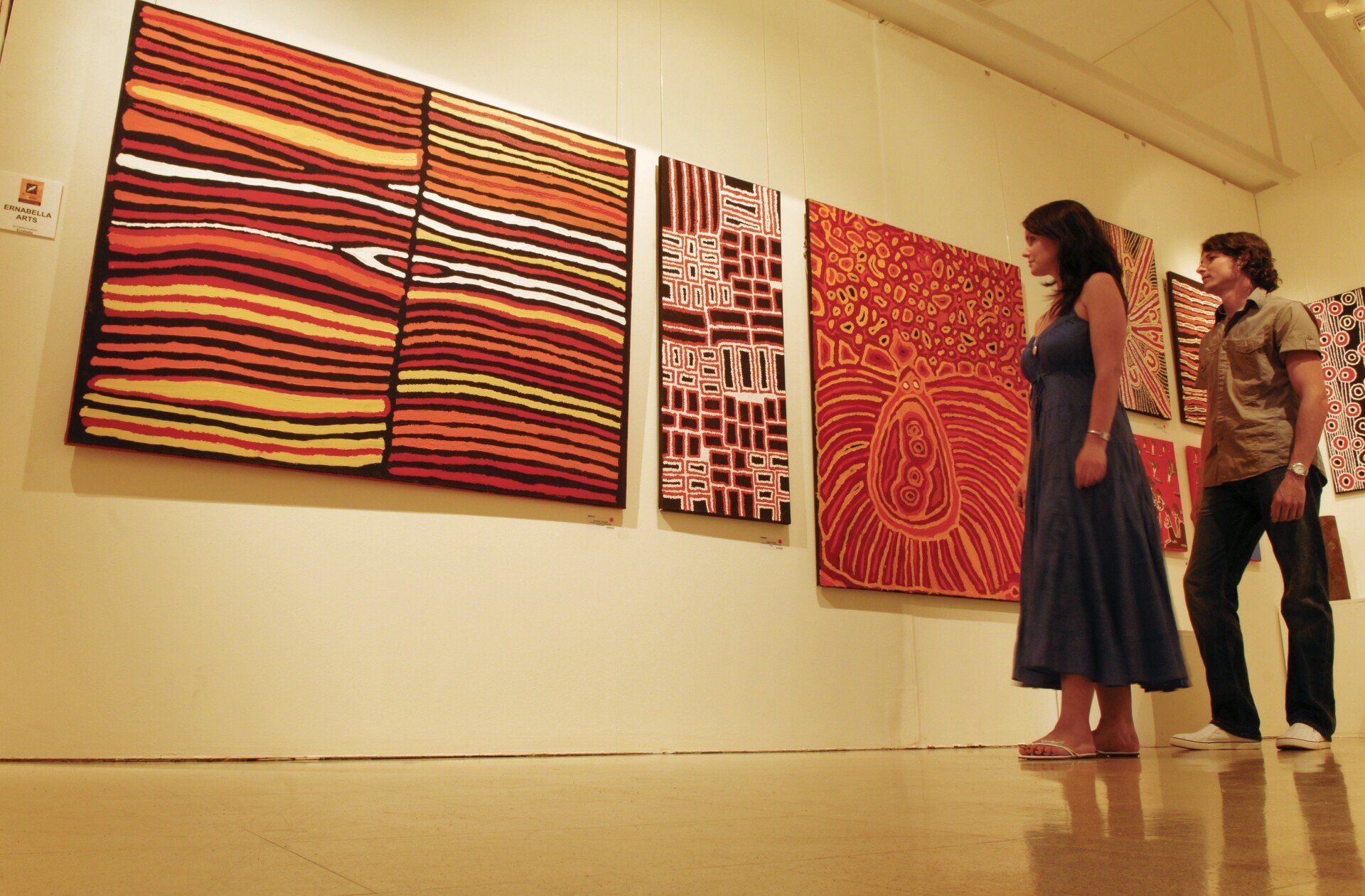 Two people are looking at paintings on a wall in a museum.